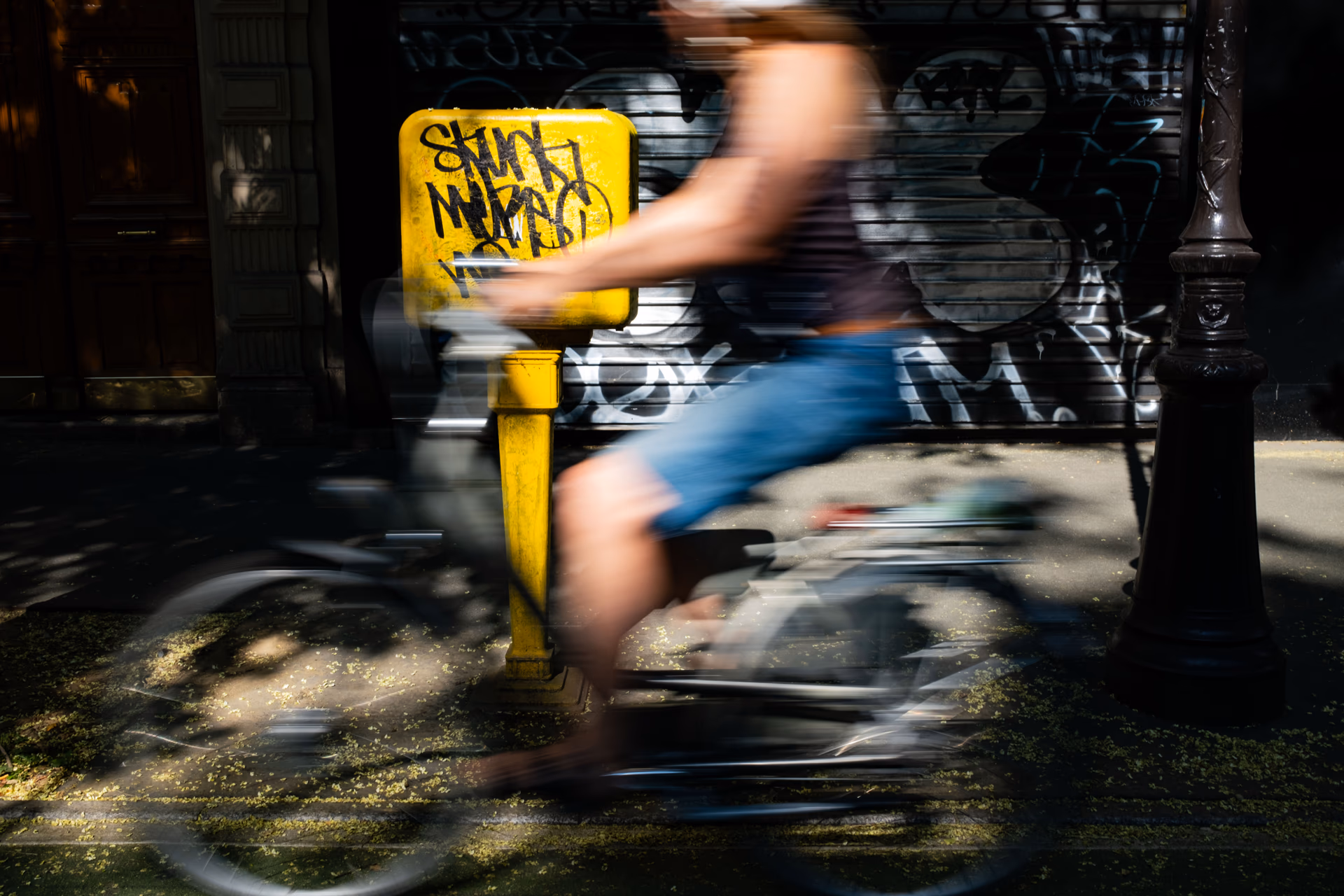 Bewegungsunschärfe: Person auf Fahrrad fährt an gelbem Poller mit Graffiti vorbei