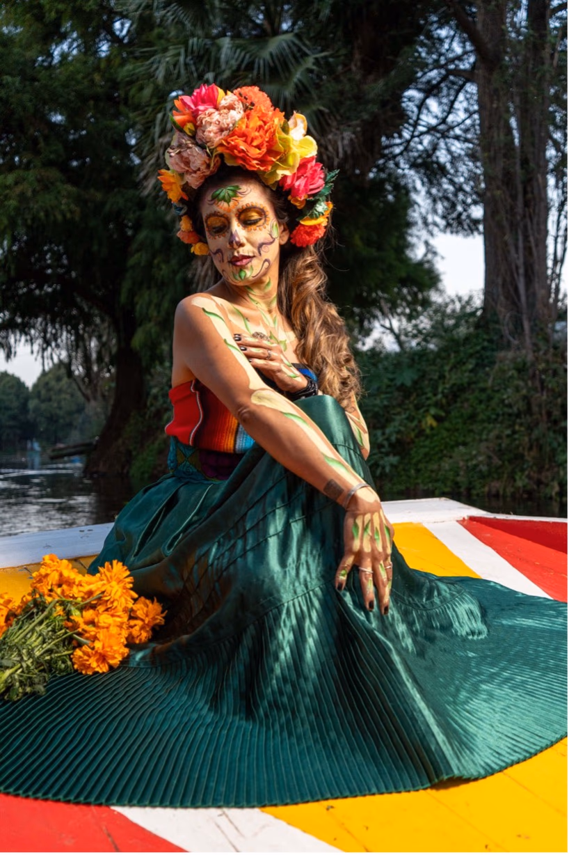 Mujer con pintura de Catrina y corona de flores sentada en una trajinera