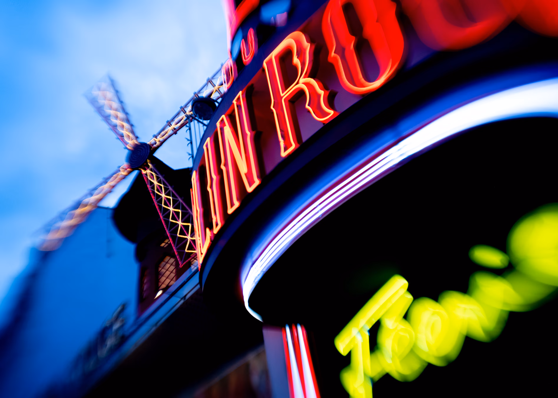 Leuchtende Neonschrift in Rot und Gelb an einer Pariser Fassade mit blauem Himmel