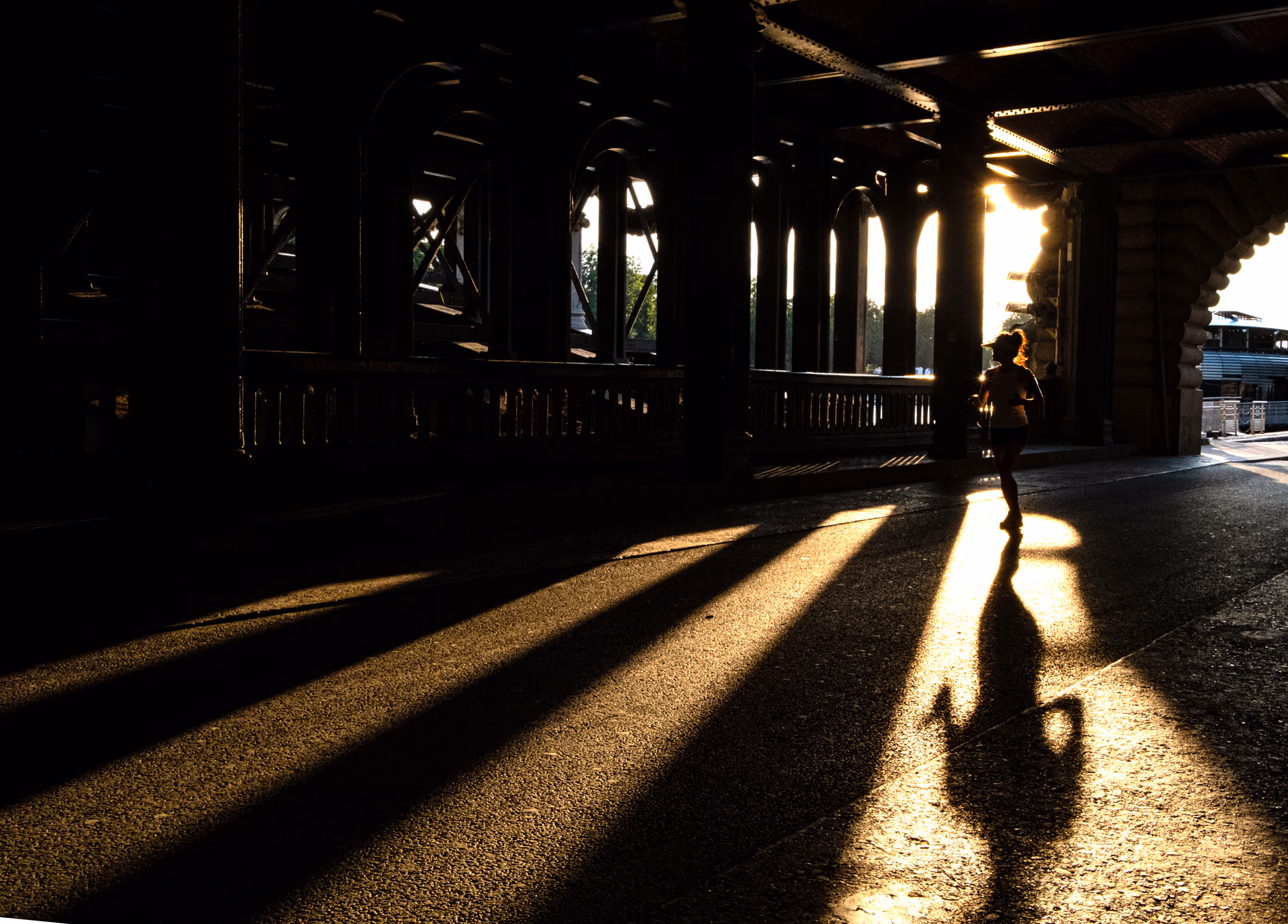 Person unter einer Brücke in dramatischem Gegenlicht mit langen Schatten auf dem Boden