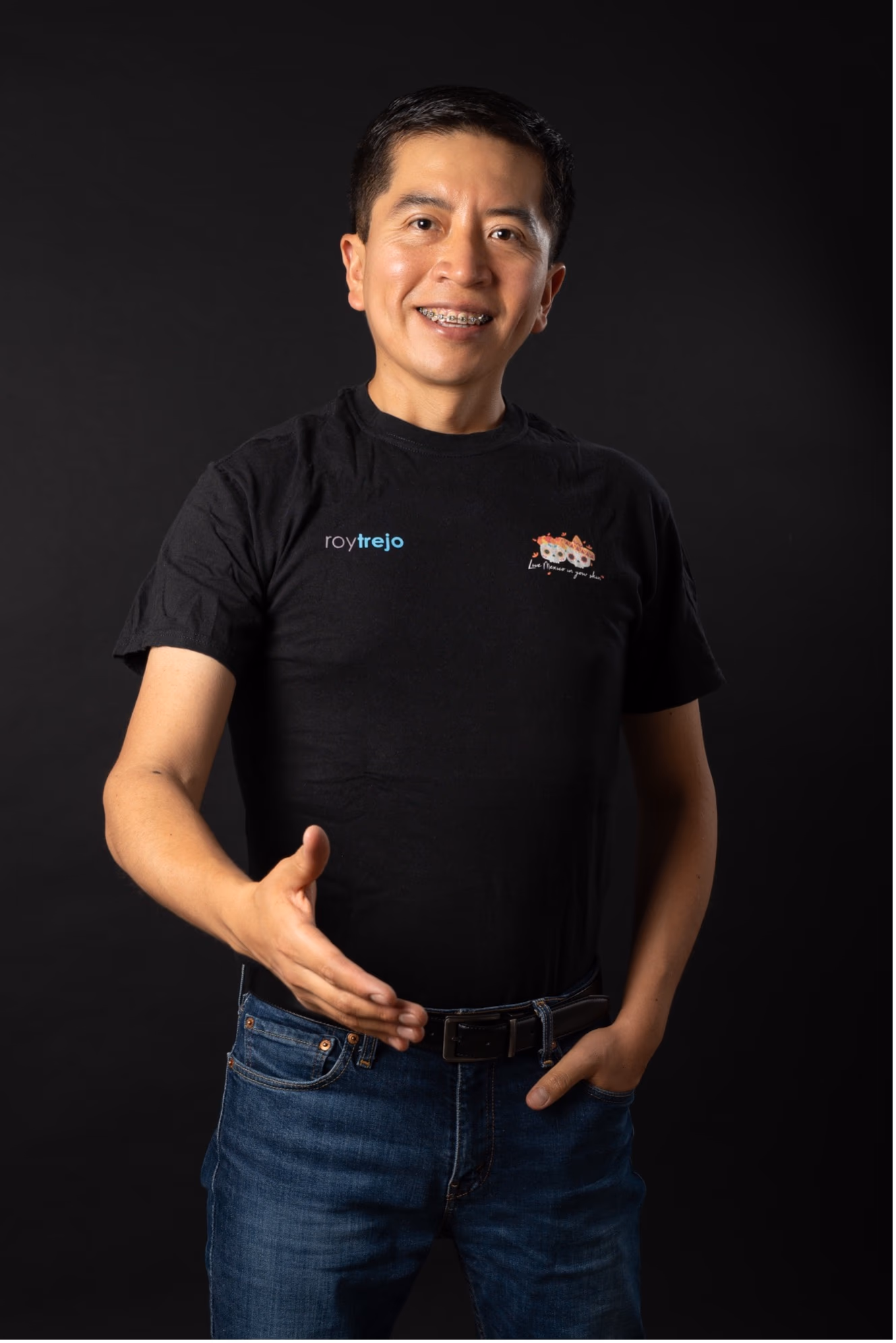 Rogelio Trejo streckt die Hand aus, trägt ein schwarzes T-Shirt mit Logo und Jeans.