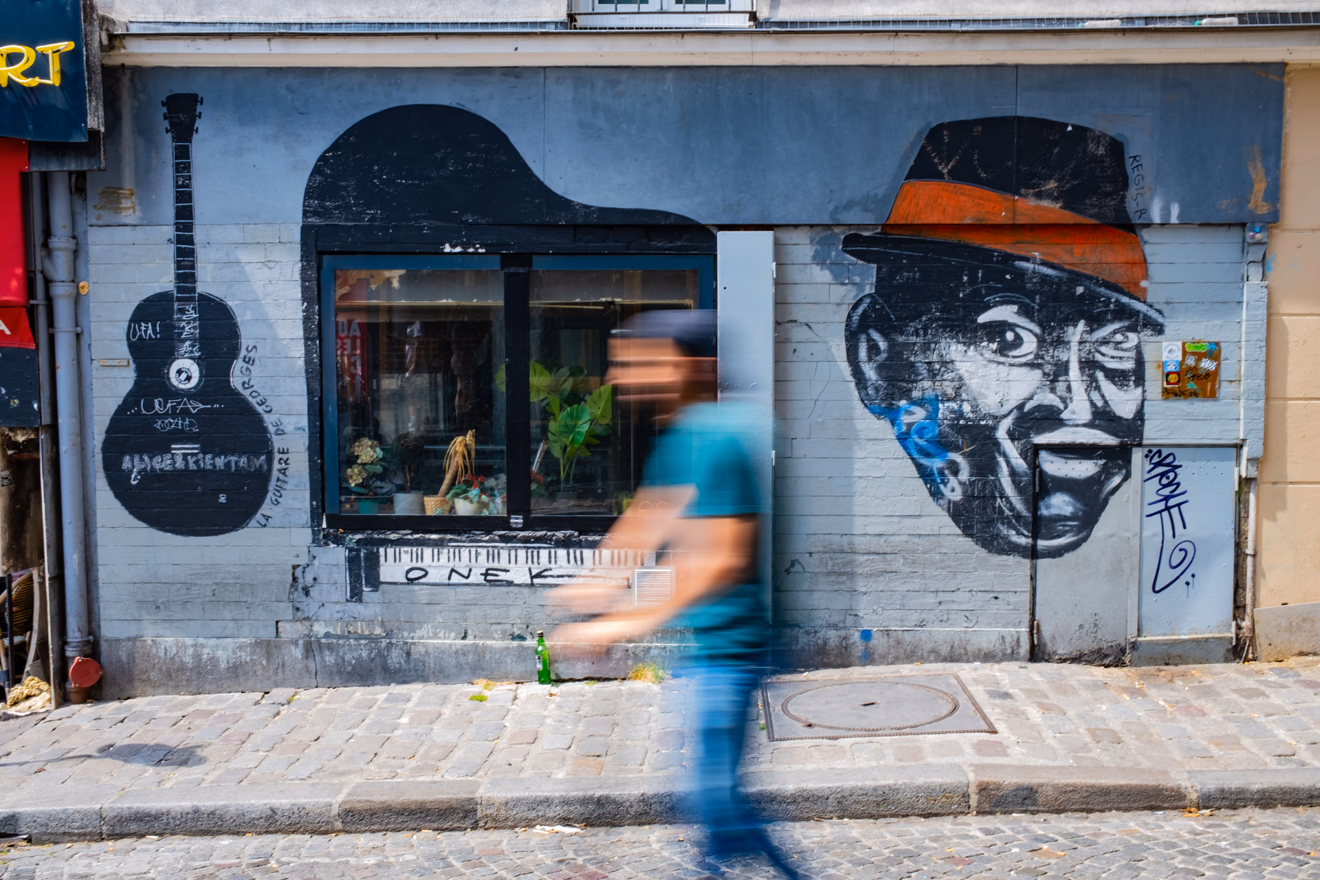 Straßenkunst an einer Hausfassade in Paris mit Graffiti und Street-Art, eine Person in blauem Shirt läuft vorbei