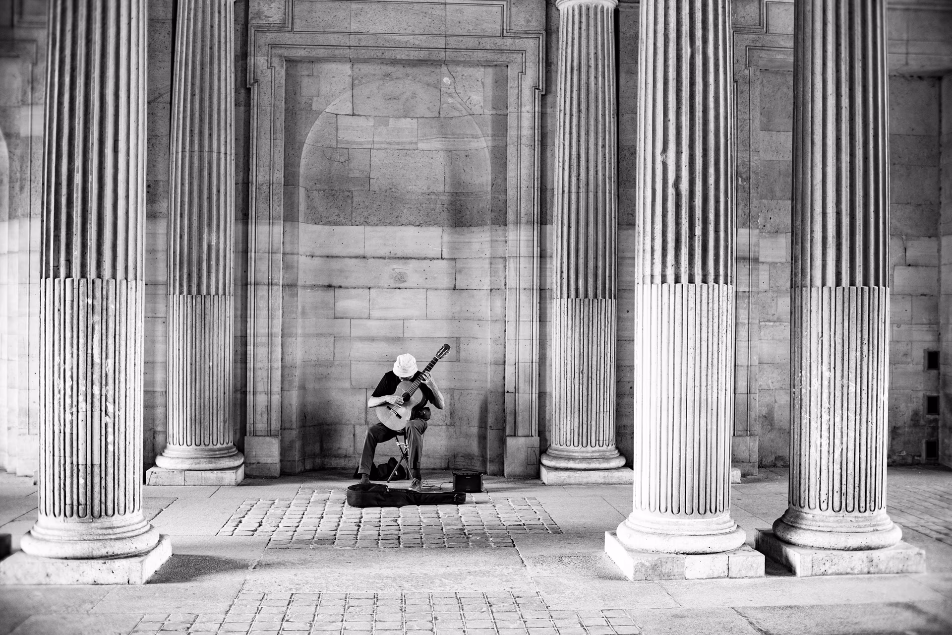 Straßenmusiker mit Gitarre sitzt zwischen klassischen Säulen in Paris