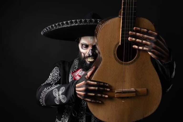 Mann mit Totenkopf-Make-up und Sombrero hält eine Gitarre, inspiriert von Catrinas am Kanal.