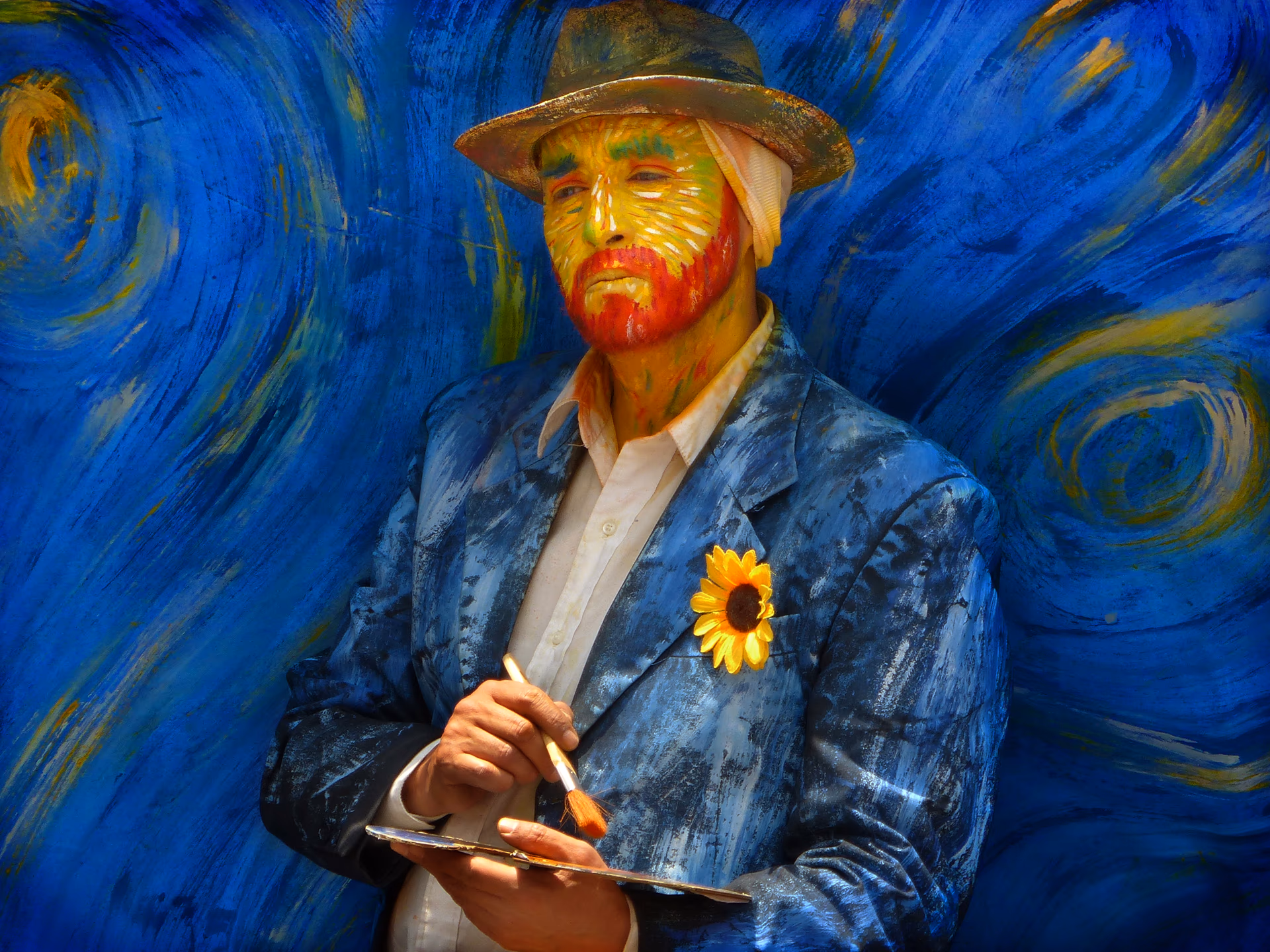 Mann mit Van-Gogh-Bemalung und Sonnenblume am Sakko hält Pinsel und Palette.