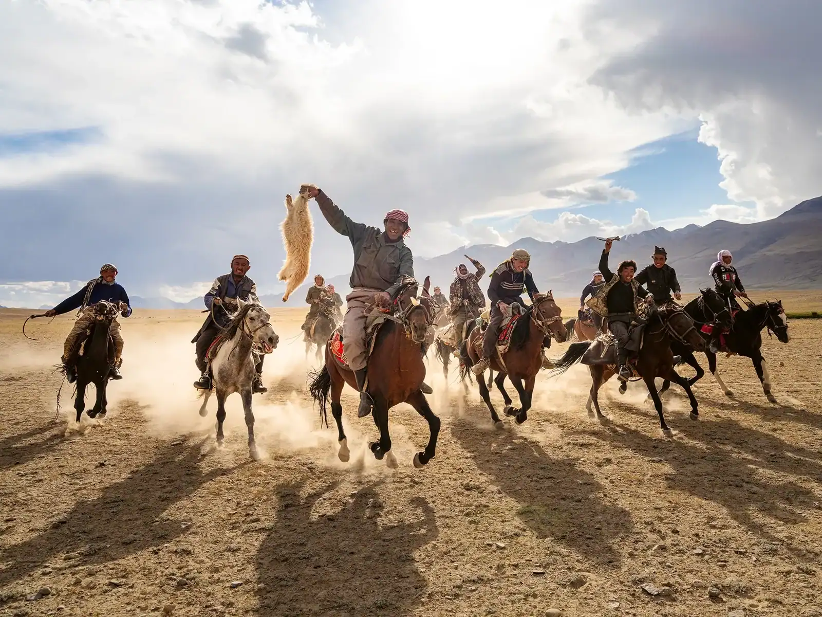 Männer reiten zu Pferd und jagen ein Tier durch staubiges Gelände.